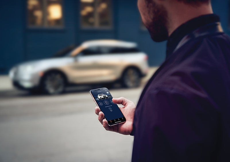 A person is shown interacting with a smartphone to connect to a Lincoln vehicle across the street. | Ted Russell Lincoln in Knoxville TN